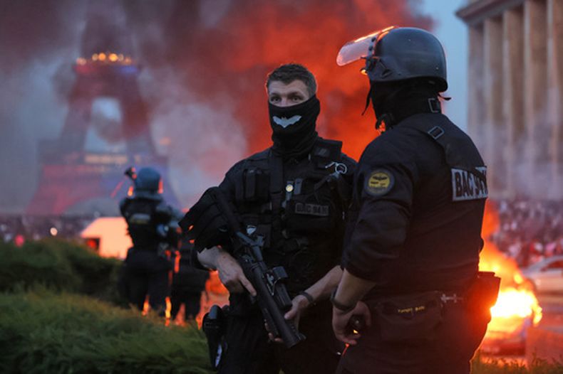 Un automóvil arde y estallan fuegos artificiales mientras la policía observa a los aficionados del PSG celebrar en París, el sábado 30 de mayo de 2026, tras el partido de fútbol de la final de la Liga de Campeones entre el París Saint-Germain y el Arsenal disputado en Budapest; el PSG ganó el encuentro. (Foto AP/Thomas Padilla)
