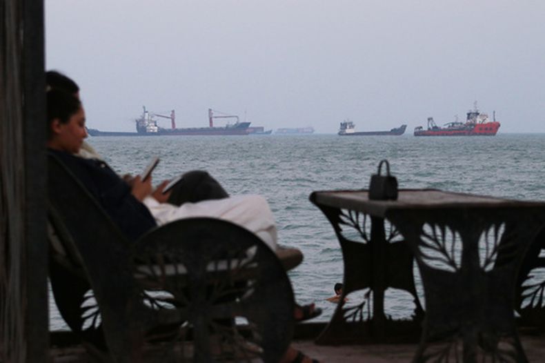 Dos personas revisan sus celulares en un café con vista a buques mercantes en el estrecho de Ormuz, el domingo 12 de julio de 2026, frente a Bandar Abbas, Irán. (Razieh Poudat/ISNA vía AP)