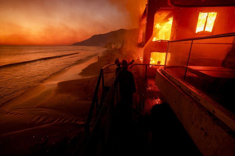 ARCHIVO - Bomberos trabajan desde una terraza mientras el incendio Palisades quema una propiedad frente a la playa el miércoles 8 de enero de 2025 en Malibú, California. (Foto AP/Etienne Laurent, archivo)