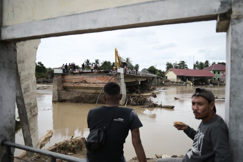 Hombres sentados cerca de un puente que se derrumbó durante una inundación repentina en Pidie Jaya, provincia de Aceh, Indonesia, el martes 2 de diciembre de 2025. (AP Foto/Reza Saifullah)