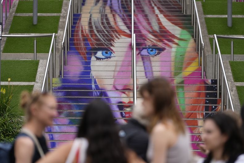 Fans posan junto a un retrato de Taylor Swift pintado en una escalera en el estadio de Wembley en Londres, el miércoles 14 de agosto de 2024, antes de una serie de conciertos de Taylor Swift que comienzan el jueves. (Foto AP/Alastair Grant)