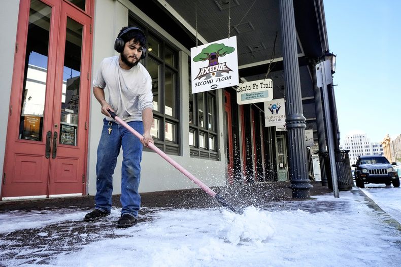Adiel Santos quita una capa de hielo de una acera frente a The Strand, mientras los negocios de la zona reabren tras una tormenta invernal, el miércoles 22 de enero de 2025, en Galveston, Texas. (Brett Coomer/Houston Chronicle vía AP)