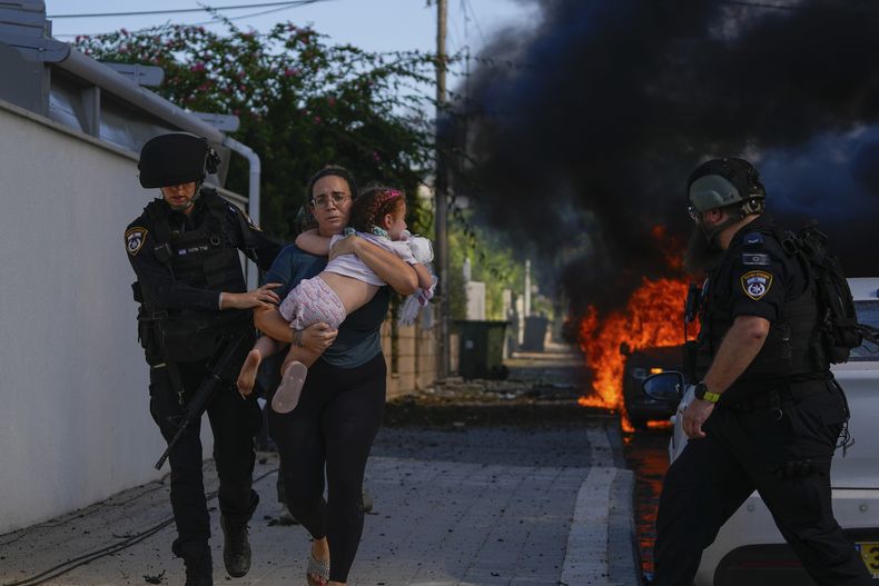 Agentes de policía evacuan a una mujer y a una niña de un lugar alcanzado por un proyectil disparado desde la Franja de Gaza, en Ashkelon, en el sur de Israel, el 7 de octubre de 2023. (AP Foto/Tsafrir Abayov)