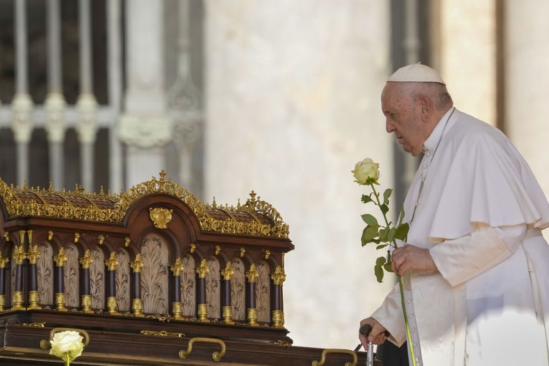 El papa Francisco, con una rosa en la mano, se dispone a rezar ante las reliquias de Santa Teresa del Niño Jesús, patrona universal de las misiones (izquierda), a su llegada a la audiencia nacional en la Plaza de San Pedro, en el Vaticano, el 7 de junio de 2023. (AP Foto/Andrew Medichini)