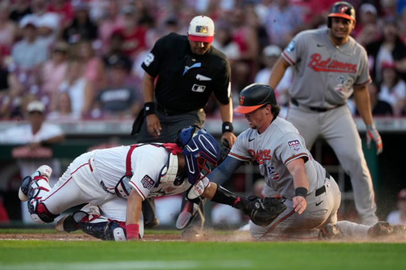 Adley Rutschman, derecha, de los Orioles de Baltimore, es puesto out por el receptor de los Rojos de Cincinnati, Jose Trevino, izquierda, durante la tercera entrada del juego de béisbol de Grandes Ligas, el sábado 4 de julio de 2026, en Cincinnati. (AP Foto/Carolyn Kaster)