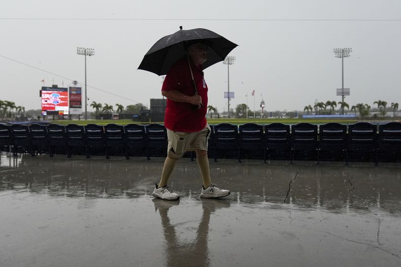 Un empleado sostiene un paraguas al caminar en el estadio de pretemporada de los Filis de Filadelfia, el lunes 24 de febrero de 2025, en Clearwater, Florida. (AP Foto/Stephanie Scarbrough)