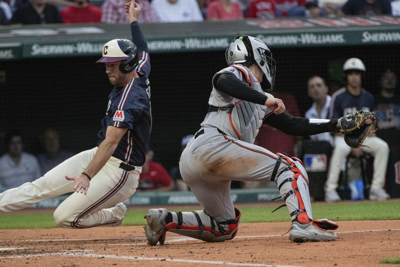 David Fry, izquierda, de los Guardianes de Cleveland, anota con un elevado de sacrificio de Austin Hedges, mientras que Adley Rutschman, de los Orioles de Baltimore, intenta sacarlo en el plato sin éxito durante la tercera entrada del juego de béisbol en Cleveland, el viernes 2 de agosto de 2024. (AP Foto/Phil Long)