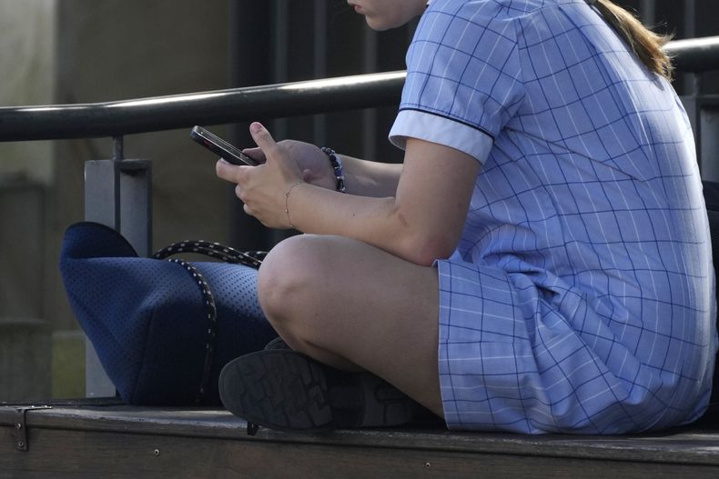 Una joven utiliza un celular sentada en un banco en Sydney, Australia, el 8 de noviembre de 2024. (AP Foto/Rick Rycroft)