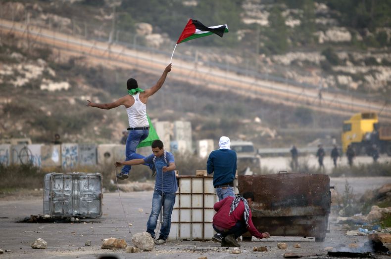 Un manifestante palestino sostiene una bandera palestina mientras salta durante enfrentamientos con soldados israel&iacute;es fuera de la prisi&oacute;n militar de Ofer, cerca de la ciudad cisjordana de Ramala, el 11 de noviembre de 2014. (Foto AP/Majdi M
