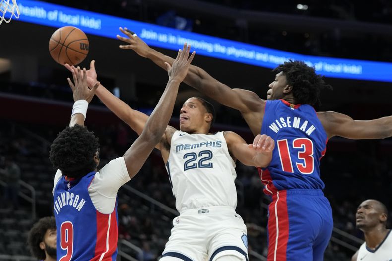 El base de los Grizzlies de Memphis Desmond Bane intenta saltar con el balón para anotar mientras lo defienden el alero Ausar Thompson y el pívot James Wiseman en el encuentro del miércoles 6 de diciembre del 2023. (AP Foto/Carlos Osorio)