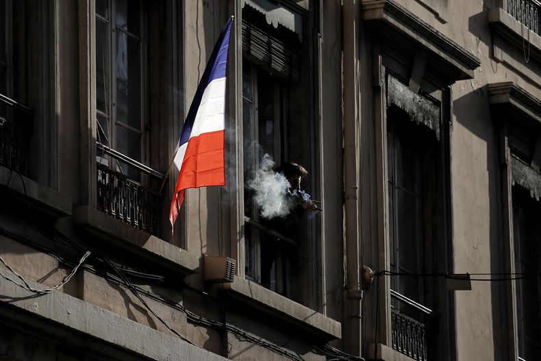 ARCHIVO - Un hombre fuma junto a una bandera francesa colgada de una ventana en Lyon, Francia, el viernes 27 de noviembre de 2015. (AP Foto/Laurent Cipriani, archivo)