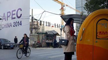 americateve | En esta imagen, tomada el 6 de noviembre de 2014, una mujer (a la derecha) compra su desayuno en un puesto callejero mientras un hombre ojea un diario en un quiosco de prensa cerca de un anuncio sobre la cumbre APEC, en Beijing, China. (Foto AP/Andy Wong)