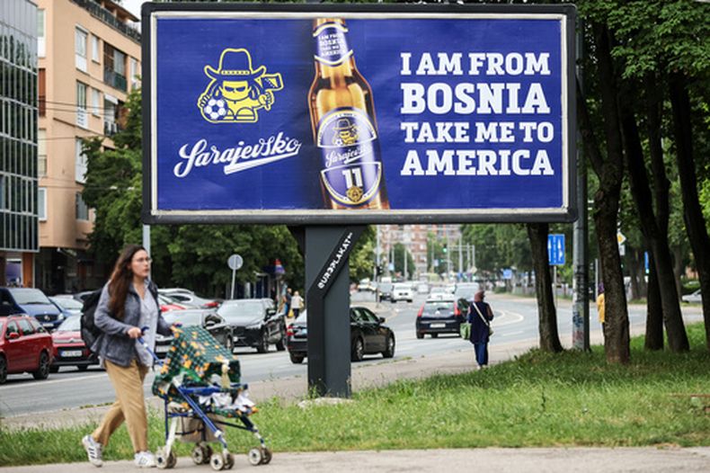 Una mujer camina frente a un cartel que despliega la letra de la canción I Am From Bosnia, Take Me to America de Dubioza en Sarajevo, Bosnia,el jueves 11 de junio de 2026. (AP Foto/Armin Durgut)