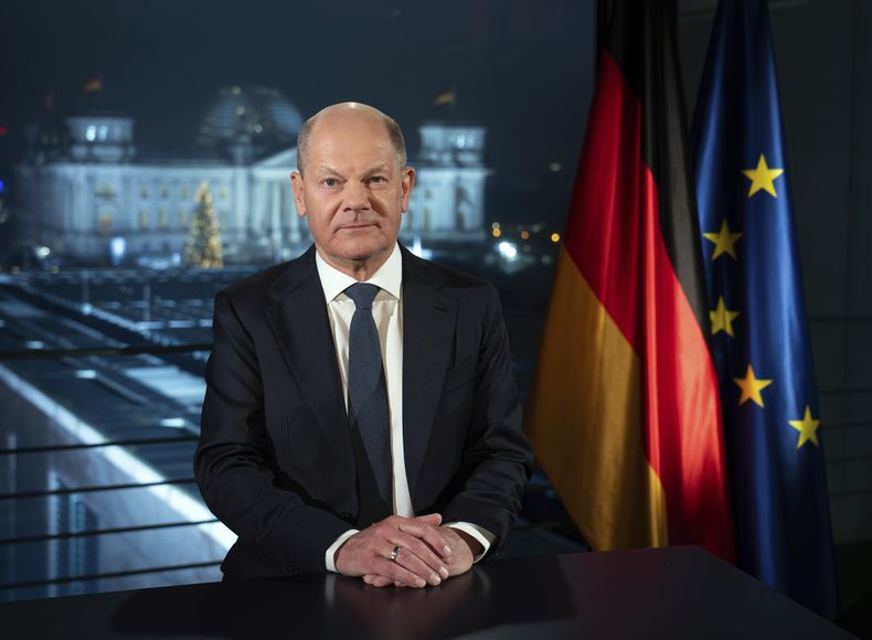 El canciller alemán, Olaf Scholz, se ve sentado con el Reichstag iluminado al fondo durante una sesión de fotos tras la grabación de su mensaje de Año Nuevo en la Cancillería, en Berlín, Alemania, el 29 de diciembre de 2024. (Soeren Stache/dpa via AP)