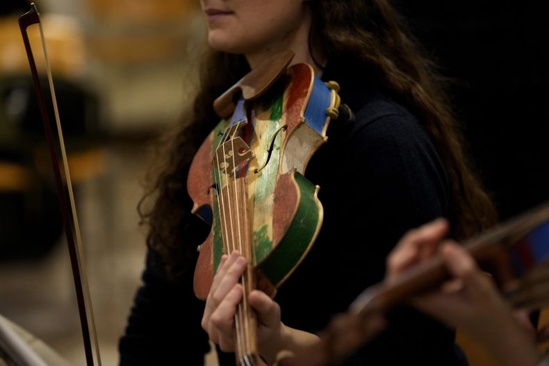 Una integrante de la Orquesta del Mar ensaya con un violín hecho con madera de barcos de inmigrantes en Milán, en el norte de Italia el sábado 10 de febrero de 2024. Reclusos de la prisión Opera de máxima seguridad usan la madera de los botes de inmigrantes para crear instrumentos musicales que la Orquesta del Mar tocó en su debut en el Teatro alla Scala (Foto AP/Antonio Calanni)