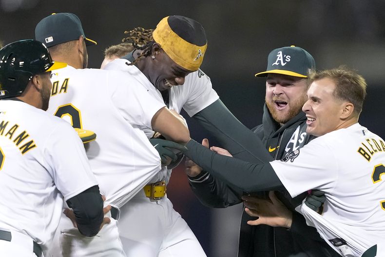 Lawrence Butler (centro), de los Atléticos de Oakland, festeja con sus compañeros tras conectar el hit del triunfo sobre los Nacionales de Washington, en la décima entrada del juego del viernes 12 de abril de 2024 (AP foto/Tony Avelar)