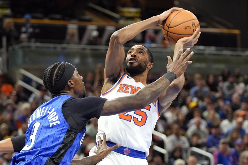 El alero de los Knicks de Nueva York, Mikal Bridges, a la derecha, realiza un disparo sobre el escolta del Magic de Orlando, Kentavious Caldwell-Pope (3), durante la primera mitad de un partido de baloncesto de la NBA, el viernes 27 de diciembre de 2024, en Orlando, Florida (AP Foto/John Raoux)