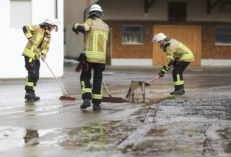 Bomberos utilizan herramientas para limpiar una calle en el pueblo de Hailtingen, afectado por inundaciones y contaminación provocadas por las fuertes lluvias en Baden-Wurttemberg, Alemania, el dmingo 7 de mayo de 2023. (Thomas Warnack/dpa via AP)
