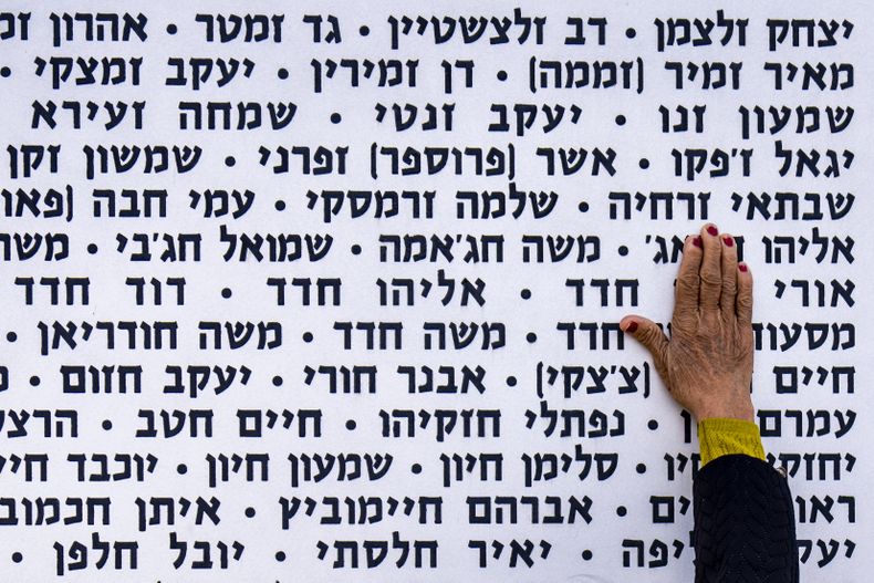Una mujer toca la pared con los nombres de soldados israelíes fallecidos en el sitio conmemorativo en Latrun, Israel, el lunes 13 de mayo de 2024. (AP Foto/Ariel Schalit)
