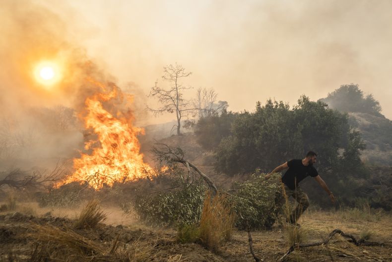 Ilias Kyriakou, de 25 años, arrastra una rama de olivo mientras un incendio quema parte de la localidad de Gennadi, en la isla de Rodas, en el sureste de Grecia, el 25 de julio de 2023. (AP Foto/Petros Giannakouris)