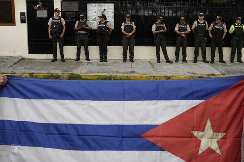 La gente ondea una bandera cubana mientras la policía hace guardia frente a la embajada de Cuba en Quito, Ecuador, el jueves 5 de marzo de 2026. (Foto AP/Carlos Noriega)