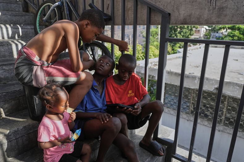 Unos niños ven una película en un dispositivo móvil, en un refugio para familias desplazadas por la violencia de las pandillas, el miércoles 19 de agosto de 2026, en Puerto Príncipe, Haití. (AP Foto/Odelyn Joseph)