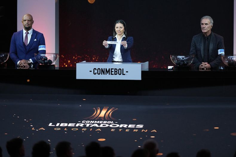 Luciana Antunes de la CONMEBOL sostiene un papel con el nombre de Boca Juniors al lado de Felipe Melo (izquierda) y Oscar Ruggeri (derecha) durante el sorteo de la Copa Libertadores, el jueves 19 de marzo de 2026, en Luque, Paraguay. (AP Foto/Jorge Saenz)