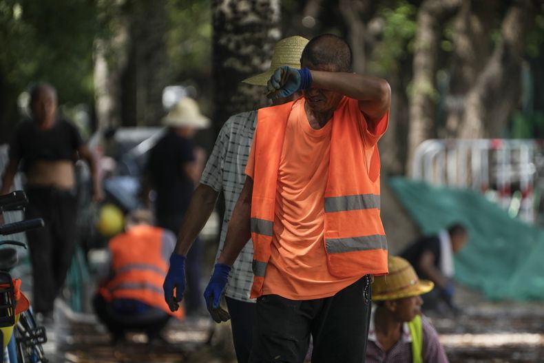 Un trabajador se seca el sudor mientras él y sus compañeros colocan baldosas en el pavimento en un día sofocante en Beijing, el lunes 10 de julio de 2023. China está padeciendo una ola de calor, inundaciones y sequía. (Foto AP/Andy Wong)
