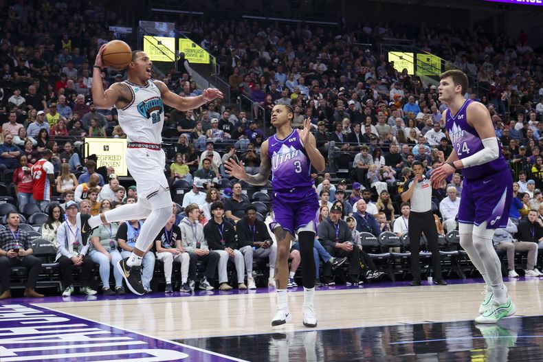 El base de los Grizzlies de Memphis Desmond Bane salta para salvar un balón que iba hacia hacia afuera frente a Keyonte George y Walker Kessler del Jazz de Utah en el encuentro del martes 24 de marzo del 2025. (AP Foto/Rob Gray)