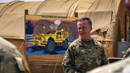 En esta imagen de la Fuerza Aérea de Estados Unidos, el general de división Kenneth P. Ekman habla delante de un cartel de Bienvenido a Niamey que muestra vehículos militares de Estados Unidos en la base aérea 101 en Níger, el 30 de mayo de 2024. (Sargento técnico Christopher Dyer, Fuerza Aérea de Estados Unidos vía AP)