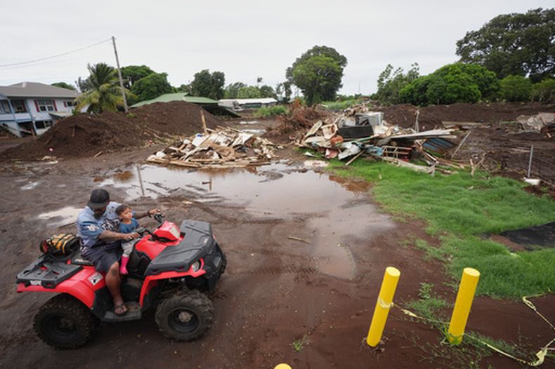 Un hombre se desplaza con su hijo cerca de una casa destruida el mes anterior al paso del huracán Lala, mientras las inundaciones del huracán Nolo retroceden, el domingo 27 de septiembre de 2026, en Naalehu, Hawai. (AP Foto/Gregory Bull)