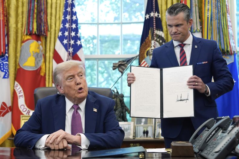 El presidente de EEUU, Donald Trump, habla mientras el secretario de Defensa, Pete Hegseth, sostiene una orden ejecutiva firmada en el Despacho Oval de la Casa Blanca, en Washington, el viernes 5 de septiembre de 2025. (AP Foto/Alex Brandon)