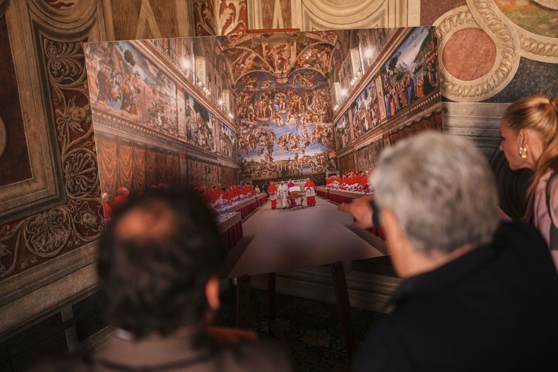 Reporteros observan una fotografía del cónclave donde fue elegido el fallecido papa Francisco el 13 de marzo de 2013, expuesta en el interior de los Apartamento Borgia, en los Museos Vaticanos, durante una visita para la prensa, el 2 de mayo de 2025. (AP Foto/Francisco Seco)