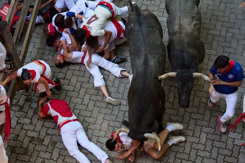 Participantes caen al suelo junto a los toros de lidia de José Escolar durante el quinto encierro de las fiestas de San Fermín, el sábado 11 de julio de 2026, en Pamplona, España. (AP Foto/Miguel Oses)