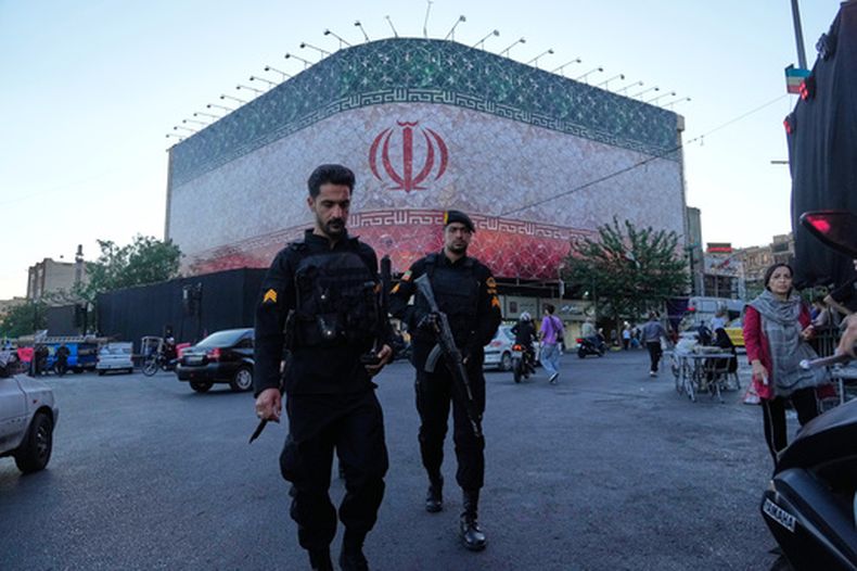 Policías caminan frente a una enorme pancarta con la bandera iraní en la plaza de la Revolución Islámica en Teherán, Irán, el domingo 14 de junio de 2026. (Foto AP/Vahid Salemi)