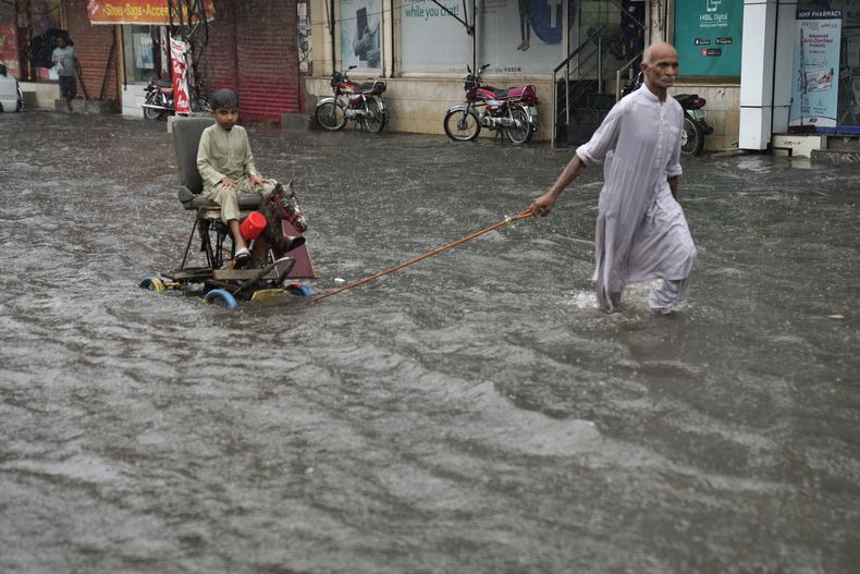 Un hombre jala una silla con un niño al recorrer una calle inundada por las lluvias en Lahore, Pakistan, el miércoles 5 de julio de 2023. (AP Foto/K.M. Chaudary)