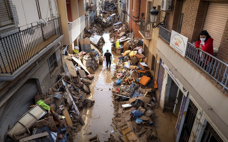 Varias personas caminan por una calle con muebles y escombros apilados a los lados de un área afectada por las inundaciones, en Paiporta, Valencia, España, el martes 5 de noviembre de 2024. (AP Foto/Emilio Morenatti)