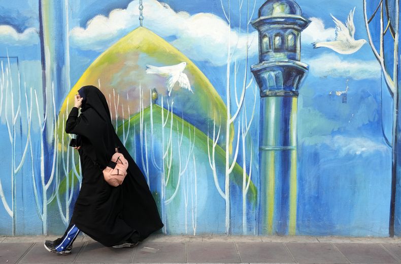 Una mujer cubierta de pies a cabeza camina frente a un mural en una mezquita del centro de Teherán, Irán, el jueves 22 de febrero de 2024. (AP Foto/Vahid Salemi)