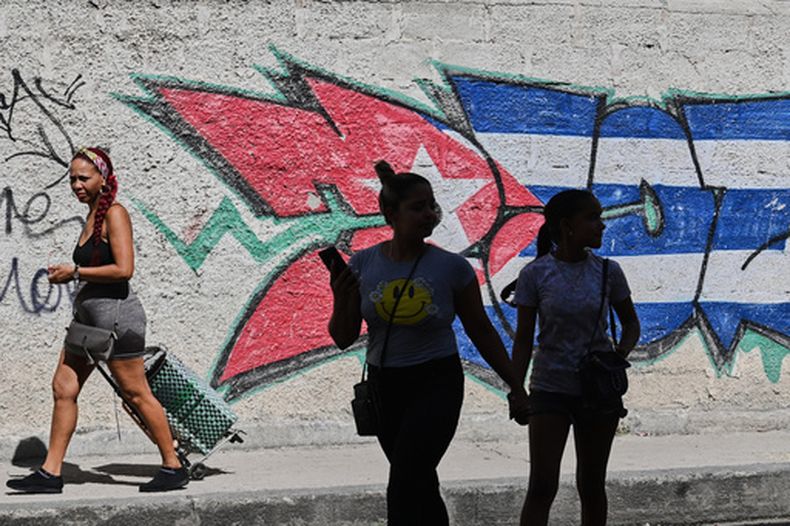 Varias personas pasan junto a grafitis con los colores de la bandera cubana en La Habana, Cuba, el miércoles 17 de junio de 2026. (Foto AP/Jorge Luis Banos)