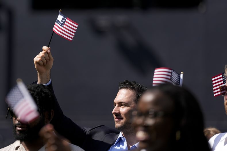 Un hombre, que forma parte de un grupo de 50 nuevos ciudadanos estadounidenses oriundos de 25 países diferentes, ondea una bandera de Estados Unidos durante una ceremonia de naturalización antes del partido de los Padres de San Diego ante los Mellizos de Minnesota, en Petco Park, el miércoles 21 de agosto de 2024, en San Diego. (AP Foto/Gregory Bull)