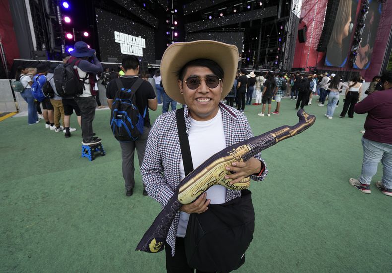 Un fan posa para un retrato un cojín con forma de rifle en el primer día del festival Arre en la Ciudad de México el sábado 9 de septiembre de 2023. (Foto AP/Fernando Llano)