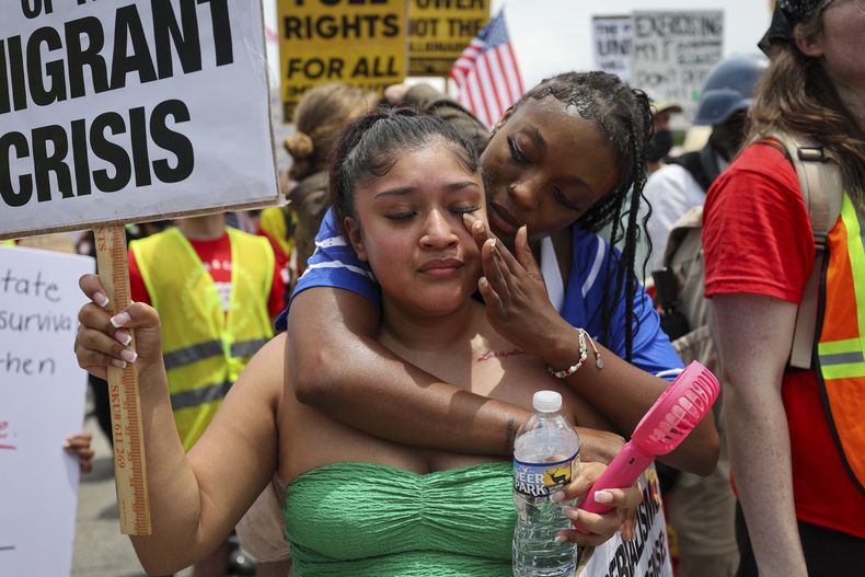 Daisy Morán, a la izquierda, y Constance Felton participan en una protesta contra las redadas del ICE y las detenciones para deportación, mientras la policía bloquea su marcha el sábado 14 de junio de 2025, en Chamblee Tucker Road, Atlanta. (Arvin Temkar/Atlanta Journal-Constitution vía AP)