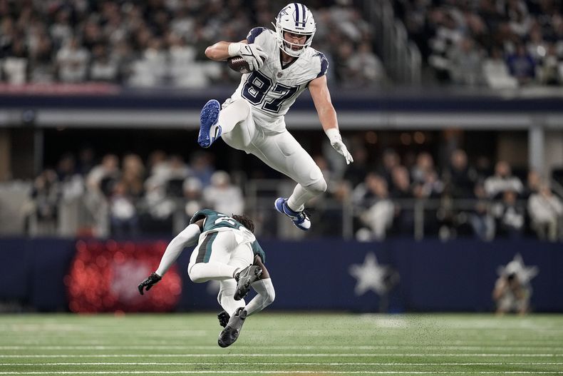 Jake Ferguson (87), tight end de los Cowboys de Dallas, brinca sobre Kelee Ringo, cornerback de los Eagles de Filadelfia, durante la segunda mitad del juego de la NFL, el domingo 10 de diciembre de 2023, en Arlington, Texas. (AP Foto/Sam Hodde)