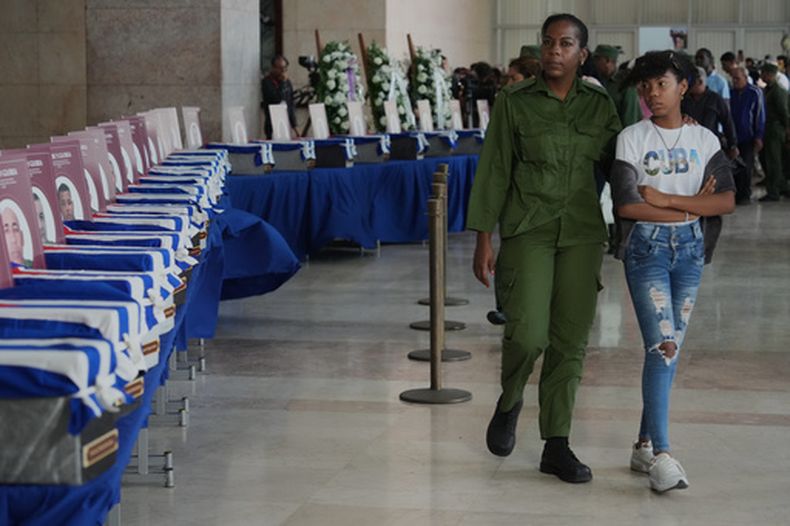 Mujeres pasan junto a las urnas con los restos de los militares cubanos que murieron durante la operación estadounidense en Venezuela para capturar al expresidente venezolano Nicolás Maduro, en el Ministerio de las Fuerzas Armadas Revolucionarias en La Habana, Cuba, el jueves 15 de enero de 2026. (Foto AP/Ramón Espinosa