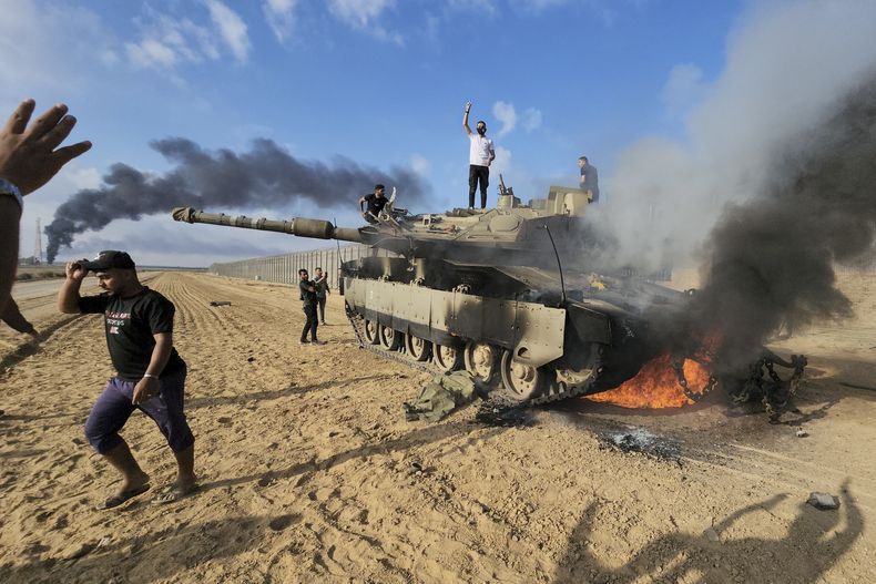 Palestinos celebran junto a un tanque israelí destruido en la cerca fronteriza de la Franja de Gaza, al este de Jan Yunis, en el sur del enclave, el 7 de octubre de 2023. Hamás, el grupo insurgente que gobierna la Franja de Gaza, llegó a cabo un ataque sin precedentes y por varios frente sobre Israel al amanecer del 7 de octubre, disparando miles de proyectiles mientras docenas de combatientes cruzaban la fortificada frontera para infiltrarse en varias localidades por tierra, mar y aire, tomando al país por sorpresa durante un importante feriado. (AP Foto)