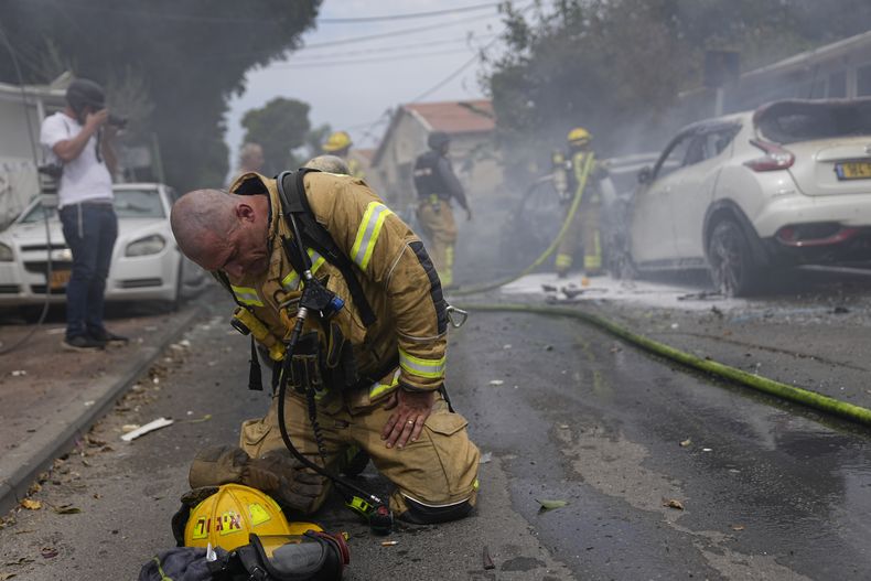 Un bombero israelí se arrodilla en el asfalto para recomponerse luego de extinguir, junto a a sus compañeros, un incendio en varios autos causado por un proyectil disparado desde la Franja de Gaza, en Ashkelon, Israel, el 9 de octubre de 2023. (AP Foto/Ohad Zwigenberg)