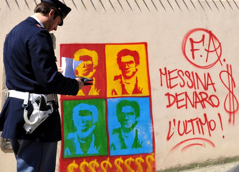 ARCHIVO - Un agente de la policía italiana observa un grafiti en el muro perimetral de la catedral de Palermo, con la imagen de Matteo Messina Denaro, en Sicilia, en el sur de Italia, el 24 de abril de 2008. (AP Foto/Alessandro Fucarini, archivo)