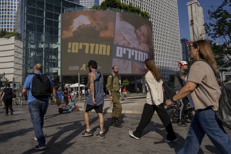 Varias personas pasan por delante de un cartel que pide la liberación de los rehenes retenidos por Hamás en Gaza desde hace casi un año, en Tel Aviv, Israel, el 10 de septiembre de 2024. (AP Foto/Ohad Zwigenberg)