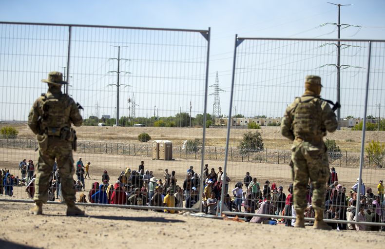 ARCHIVO - Gran cantidad de migrantes aguardan el miércoles 10 de mayo de 2023 junto a la cerca fronteriza para entrar en El Paso, Texas, ante la mirada de miembros de la Guardia Nacional del estado. (AP Foto/Andrés Leighton, archivo)