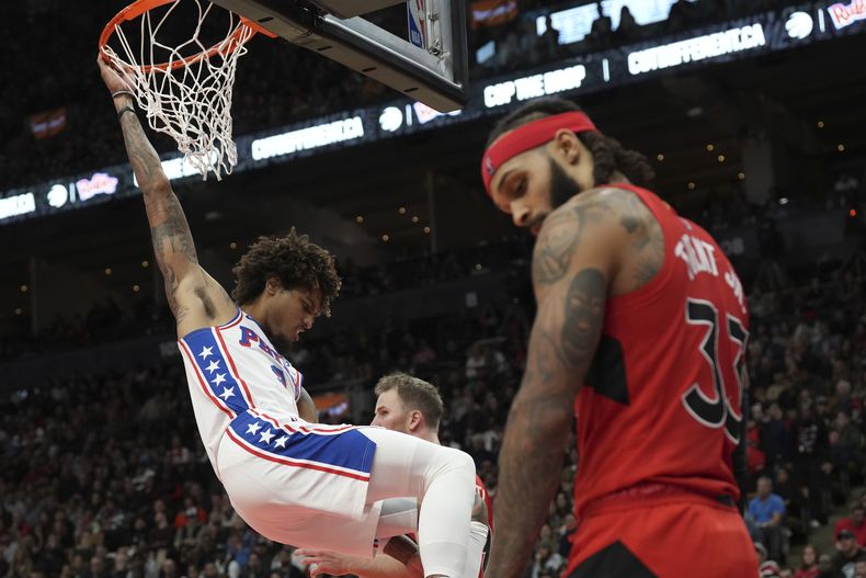Kelly Oubre, de los 76ers de Filadelfia, cuelga del aro, cerca de Gary TRent, de los Raptors de Toronto, durante el duelo del sábado 28 de octubre de 2023 (Chris Young/The Canadian Press via AP)